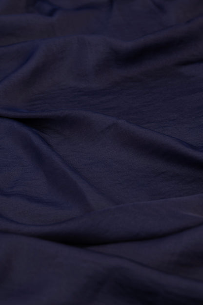 A close-up of draped dark navy blue fabric with soft folds and a slightly textured surface.