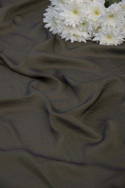 A draped piece of dark olive green fabric with soft folds, styled with a cluster of white daisies in the upper right corner.