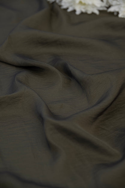A close-up of draped dark olive green fabric with soft folds and a small cluster of white flowers at the top edge.