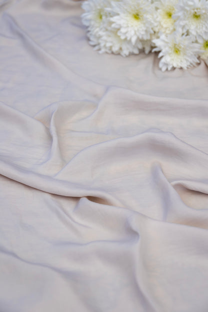 A close-up of draped pale blush pink fabric with soft folds, styled with a small cluster of white daisy-like flowers in the upper right corner.