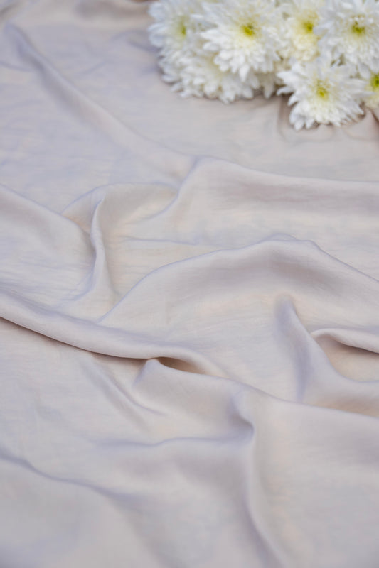 A close-up of draped pale blush pink fabric with soft folds, styled with a small cluster of white daisy-like flowers in the upper right corner.