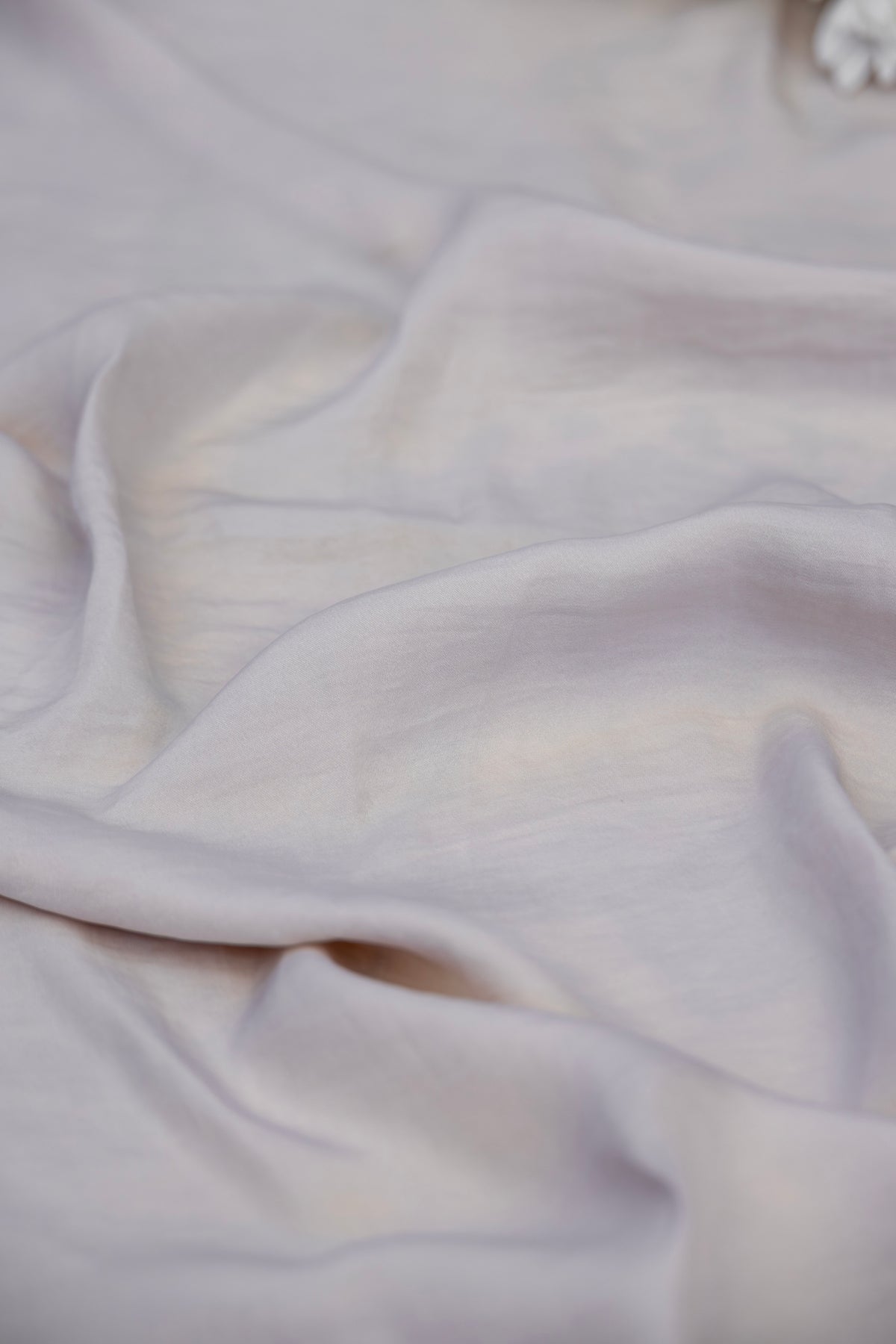 A close-up of draped light-colored fabric with soft folds and a subtle warm off-white or pale blush tone.