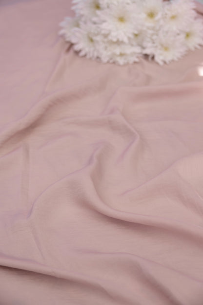 A close-up of draped dusty pink fabric with soft folds, topped near the top edge by a small cluster of white daisy-like flowers.