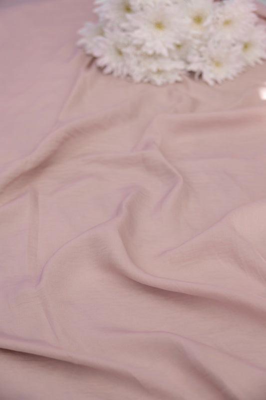 A close-up of draped dusty pink fabric with soft folds, topped near the top edge by a small cluster of white daisy-like flowers.