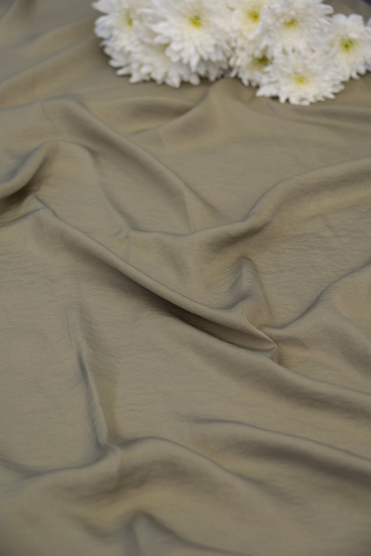 A close-up of draped fabric in a muted taupe-beige color, with a cluster of white daisies placed at the top edge as a decorative prop.
