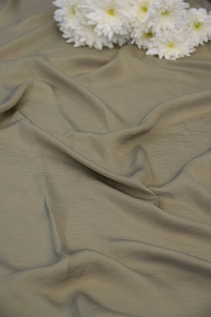A close-up of draped fabric in a muted taupe-beige color, with a cluster of white daisies placed at the top edge as a decorative prop.