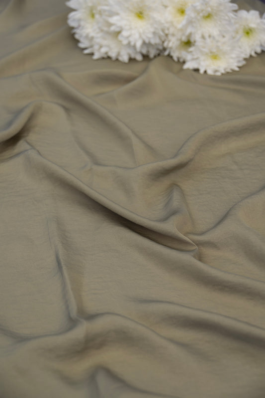 A close-up of draped fabric in a muted taupe-beige color, with a cluster of white daisies placed at the top edge as a decorative prop.