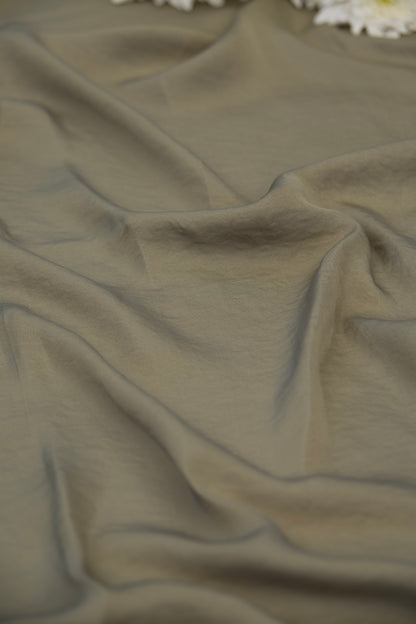 A close-up of draped olive green fabric with soft folds and a few white flowers visible at the top edge.