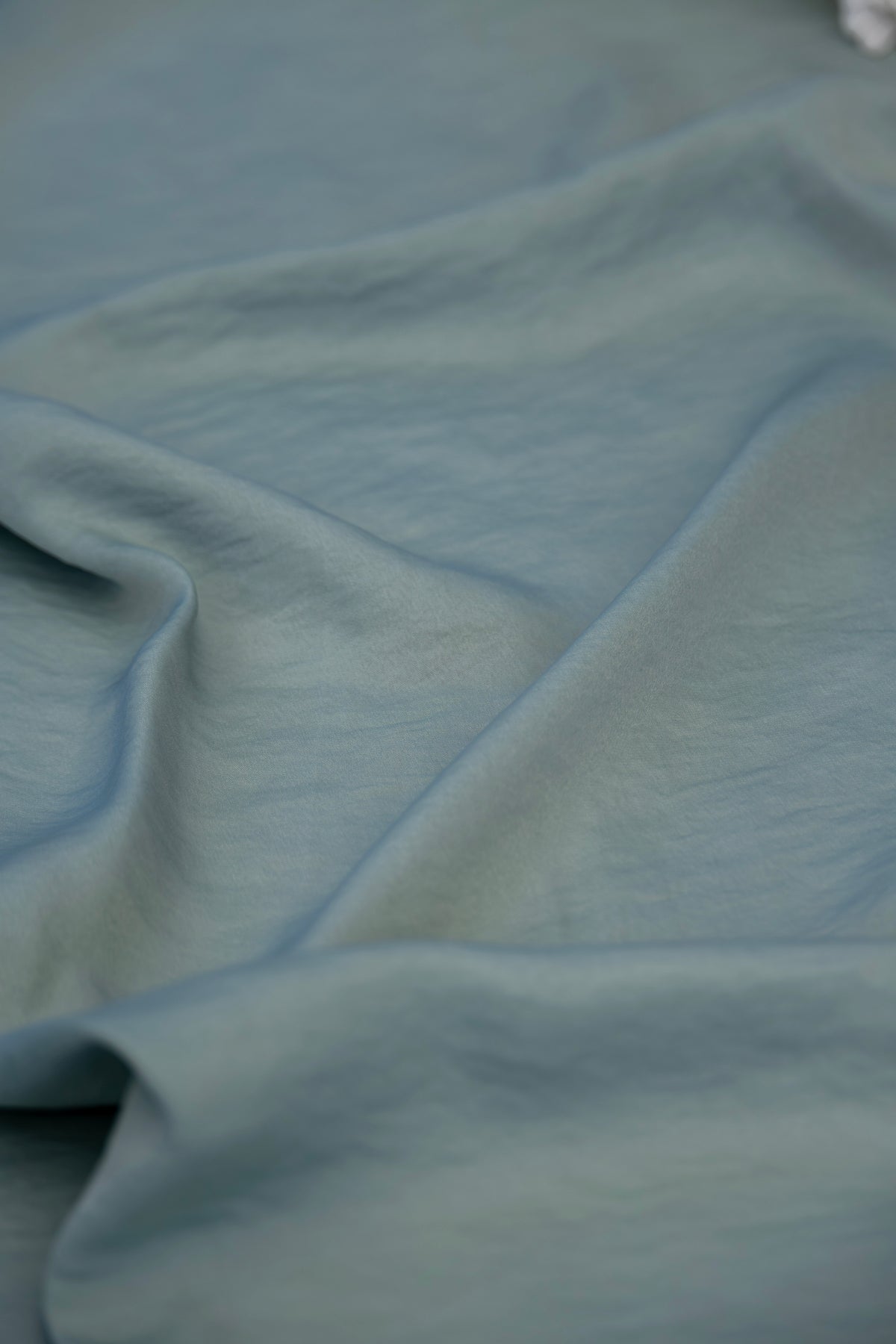 A close-up of draped dusty blue fabric with soft folds and a smooth texture.