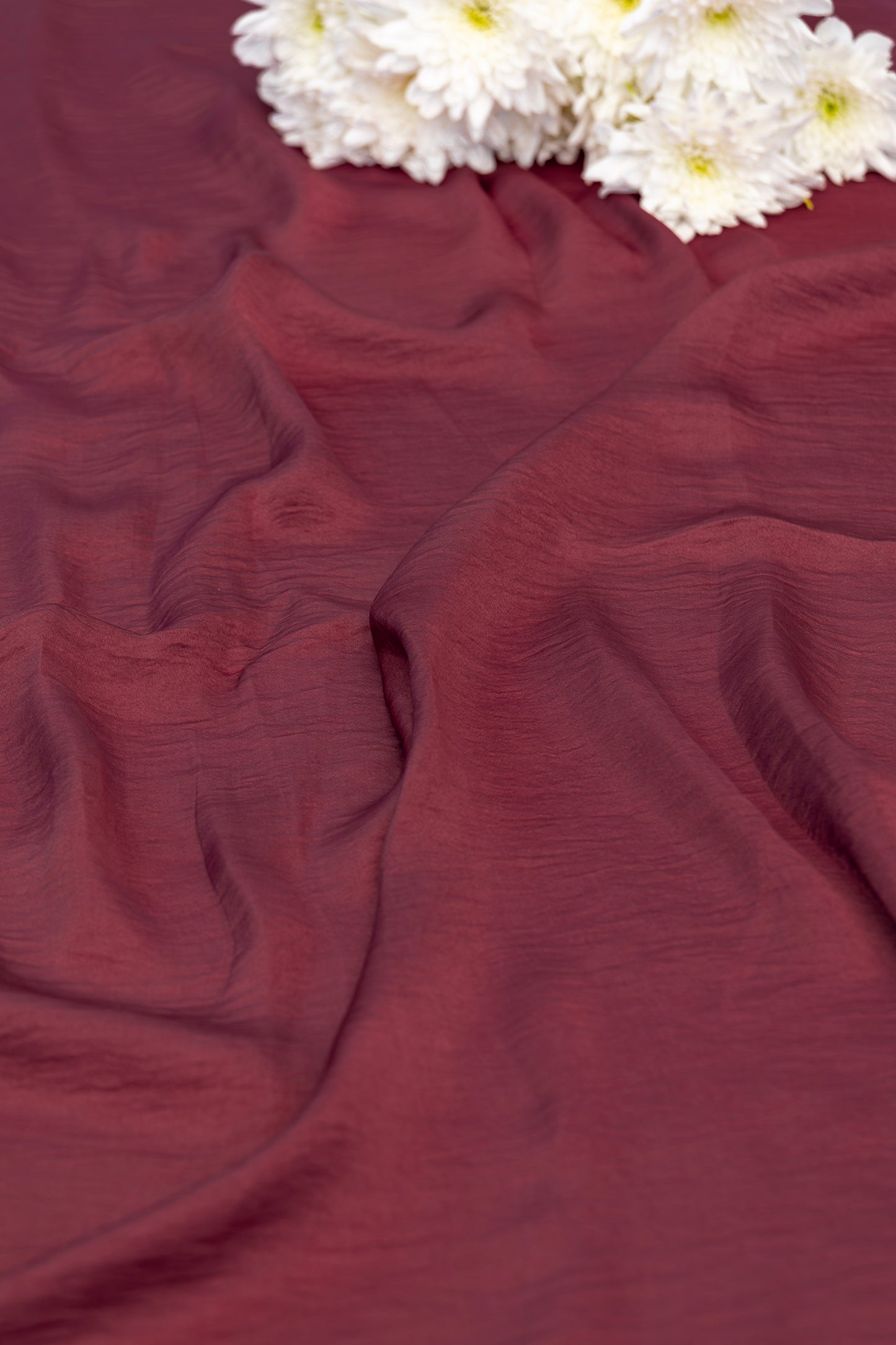 A close-up of draped burgundy fabric with white daisies placed in the top corner.