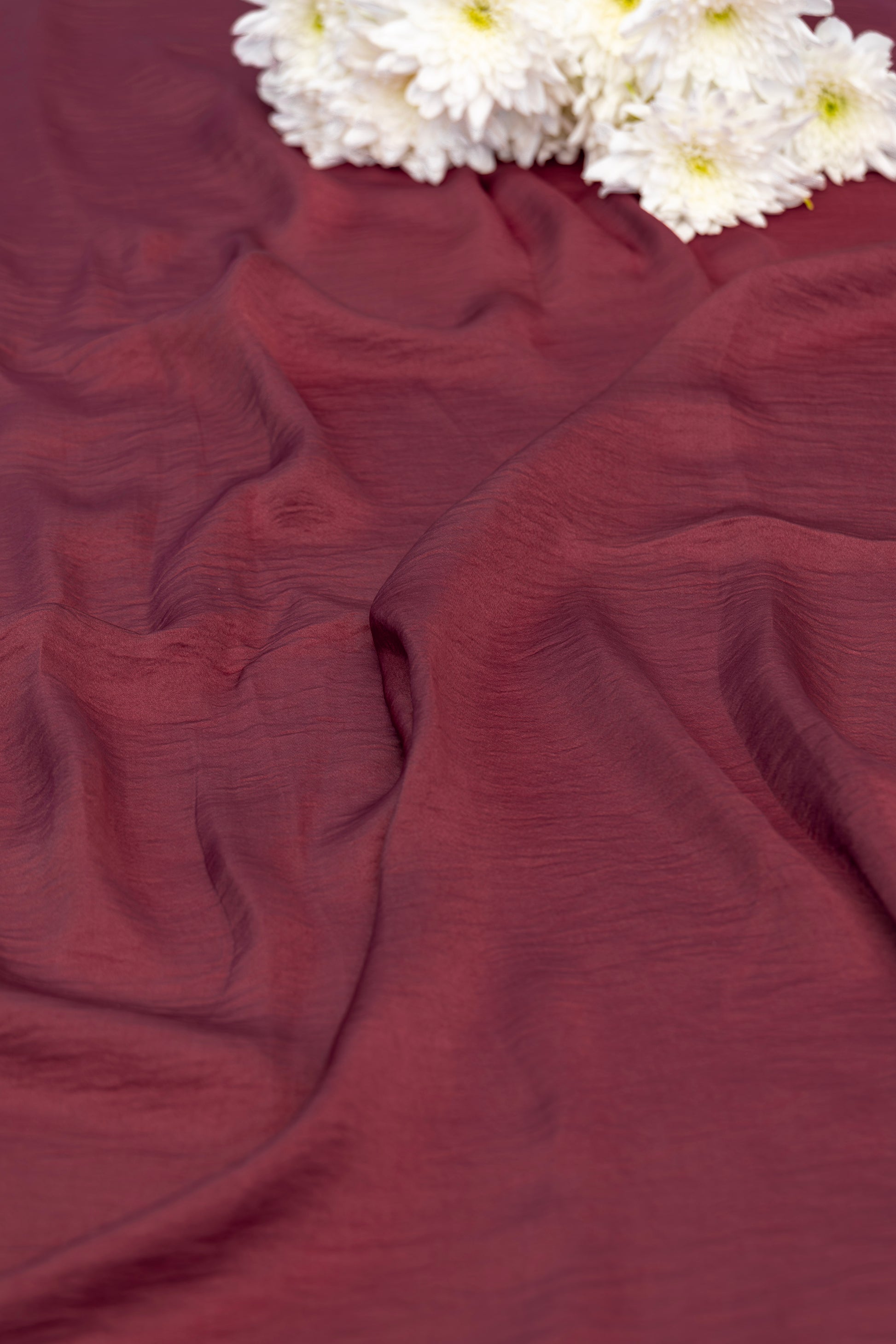 A close-up of draped burgundy fabric with white daisies placed in the top corner.