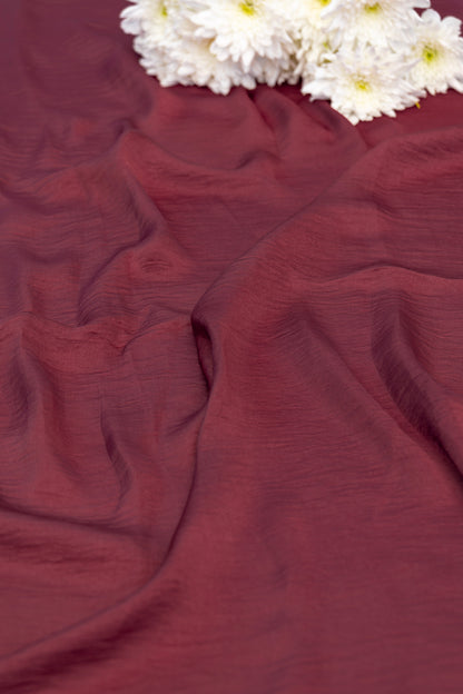 A close-up of draped burgundy fabric with white daisies placed in the top corner.