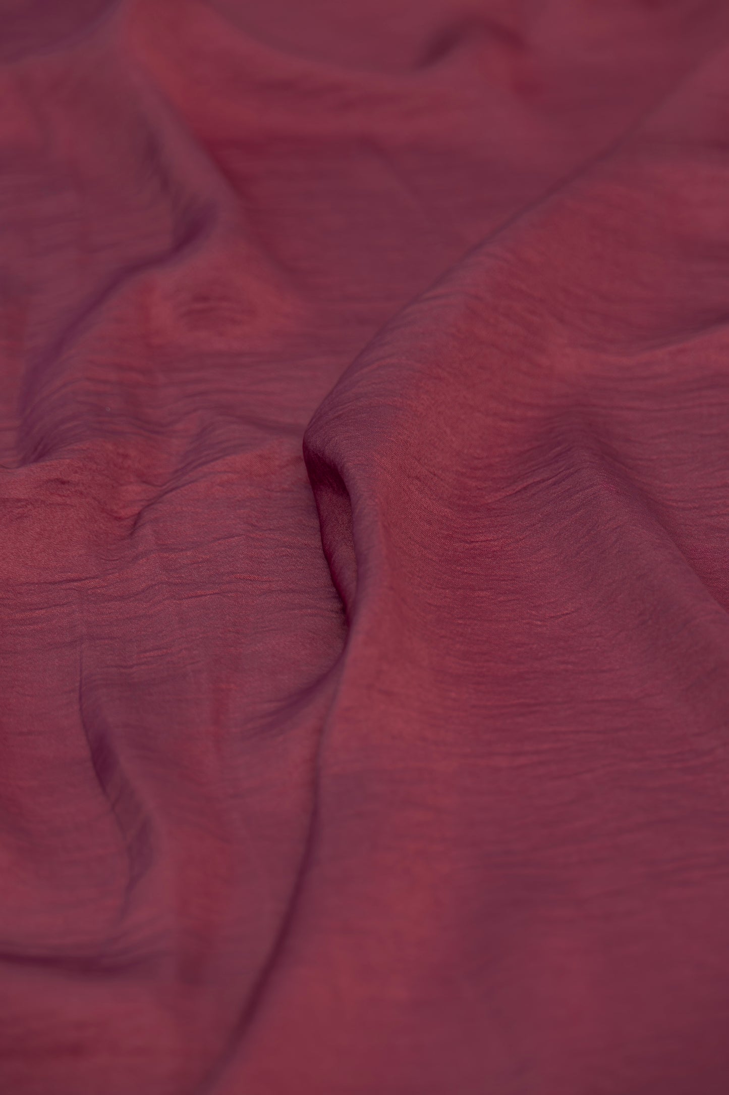 A close-up of draped dusty rose or mauve fabric with a subtle crinkled texture.