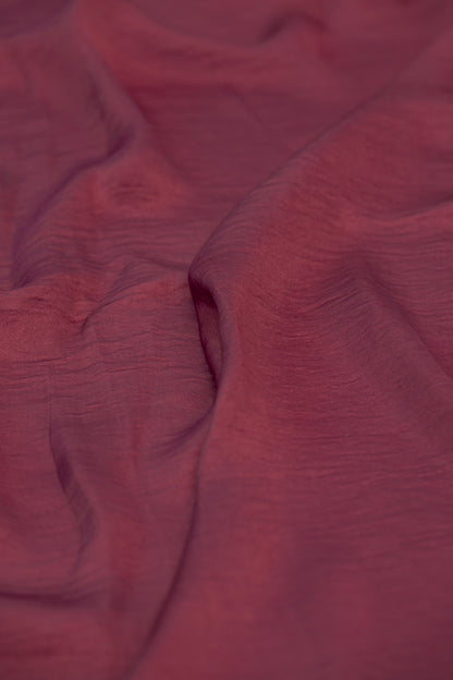A close-up of draped dusty rose or mauve fabric with a subtle crinkled texture.