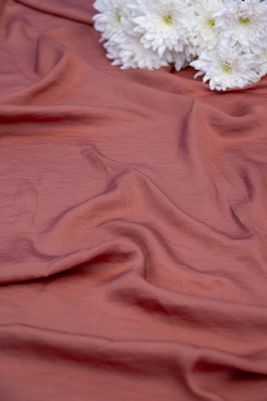 A draped dusty rose fabric with soft folds, styled with a small cluster of white flowers in the top right corner.