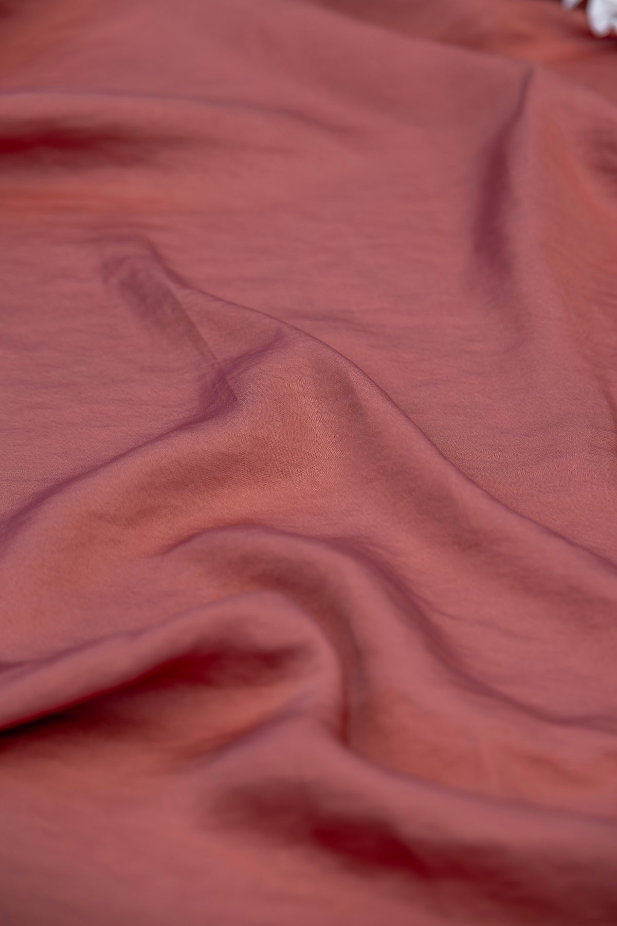 A close-up of draped dusty rose fabric with soft folds and a smooth texture.