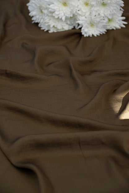 A close-up of draped brown fabric with soft folds and a small cluster of white flowers placed in the upper corner.