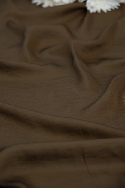 A close-up of draped brown fabric with soft folds and a small white textured accent visible at the top edge.