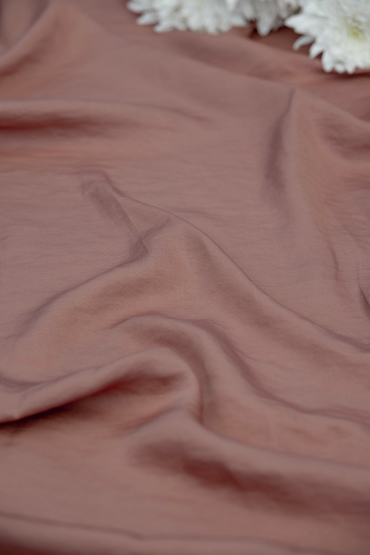 A close-up of draped dusty rose fabric with soft folds and a small cluster of white flowers at the top edge.