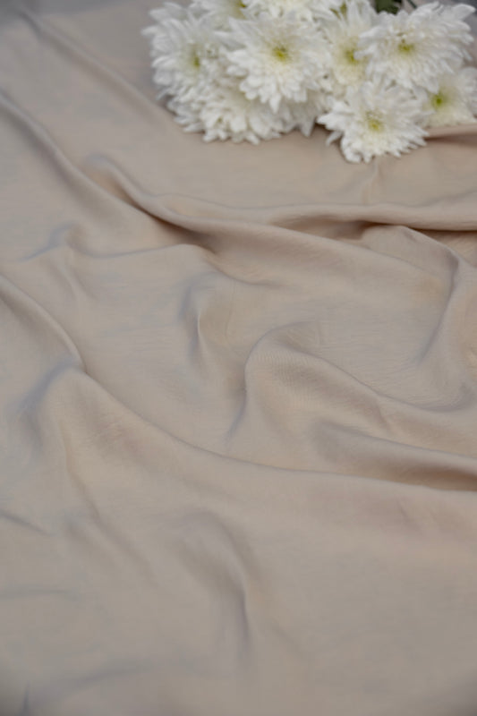 A draped piece of light beige fabric with soft folds, styled with a cluster of white chrysanthemum flowers in the upper right corner.