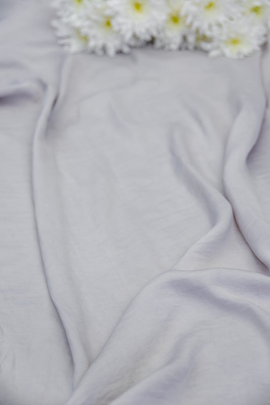 A close-up of draped light gray fabric with soft folds and a cluster of white daisies with yellow centers at the top edge.