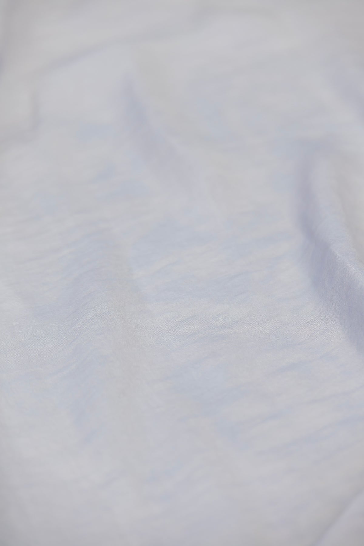 A close-up of a light-colored fabric with a soft, slightly textured surface and subtle cool-toned shadows.