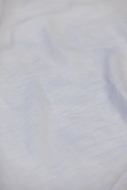 A close-up of a light-colored fabric with a soft, slightly textured surface and subtle cool-toned shadows.