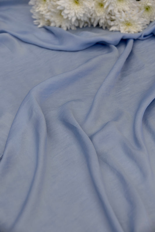 Light blue draped fabric with soft folds and a small cluster of white flowers at the top edge.