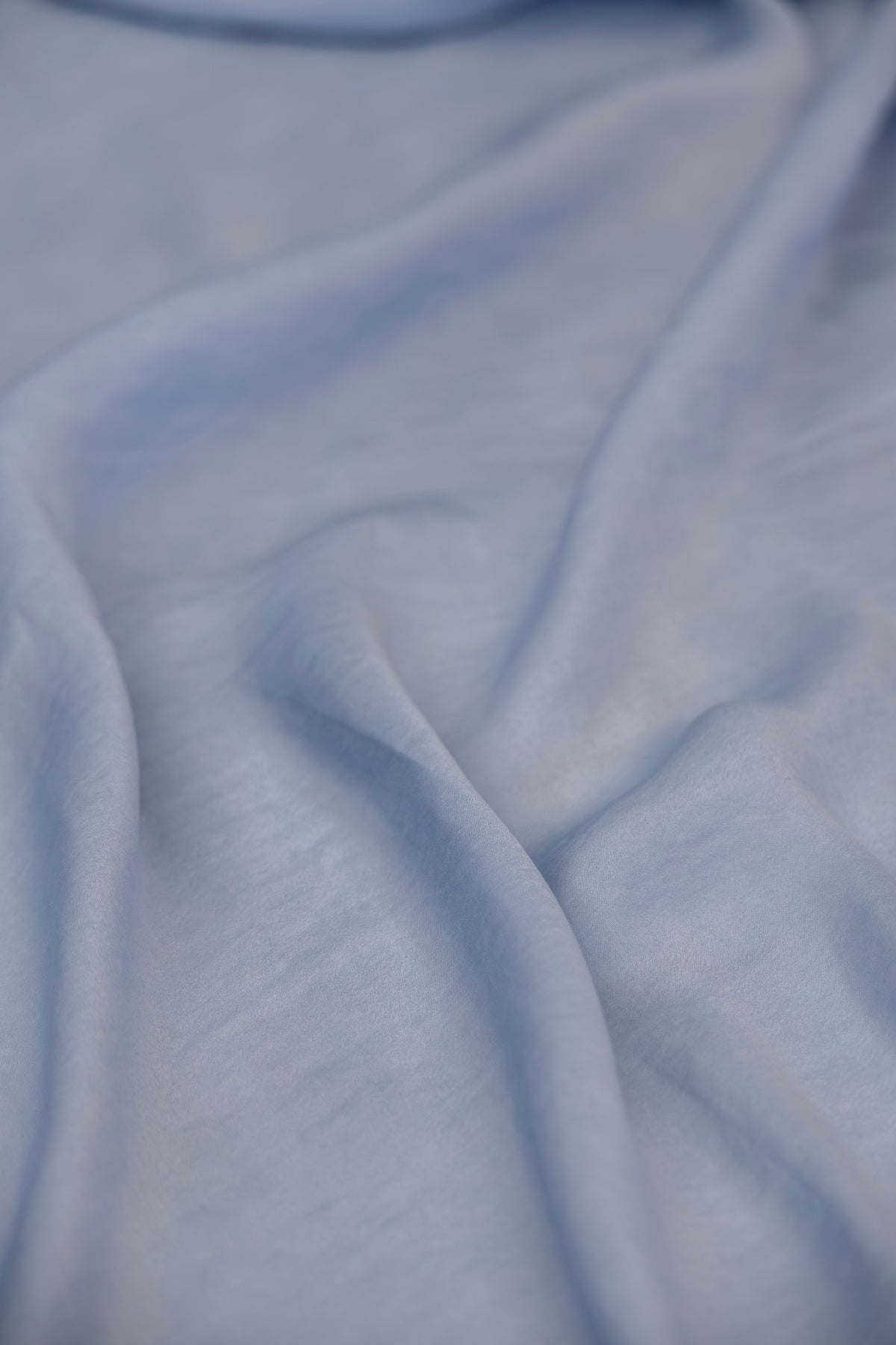 A close-up of draped light blue fabric with soft folds and a smooth texture.