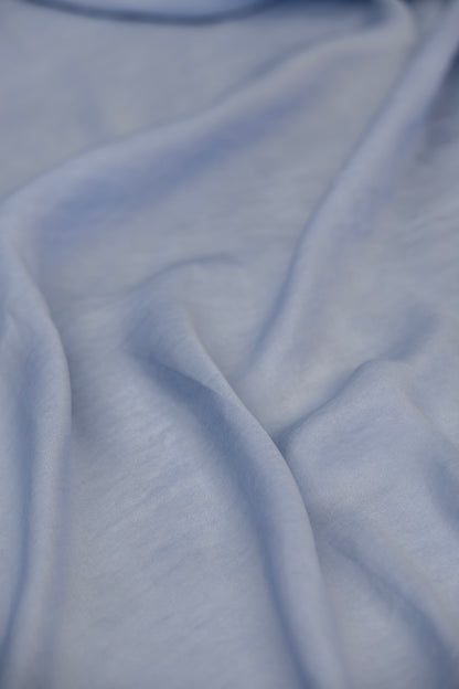 A close-up of draped light blue fabric with soft folds and a smooth texture.