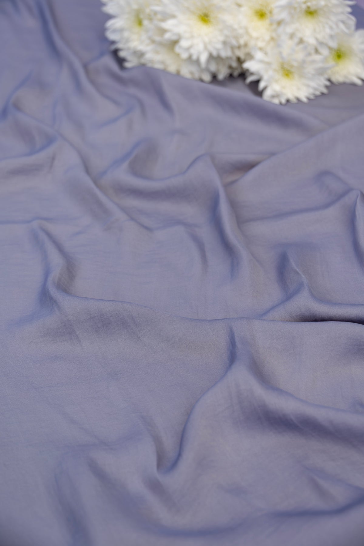 A draped piece of dusty lavender-blue fabric with soft folds, styled with a cluster of white daisies in the top right corner.