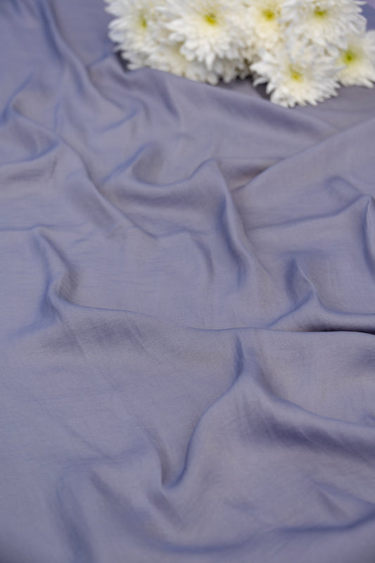 A draped piece of dusty lavender-blue fabric with soft folds, styled with a cluster of white daisies in the top right corner.