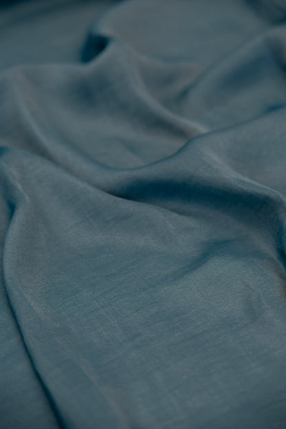 A close-up of draped slate blue fabric with soft folds and a subtle woven texture.