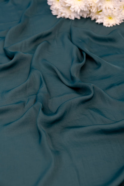 A close-up of draped teal green fabric with soft folds, styled with white dried flowers in the upper corner.