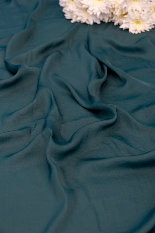 A close-up of draped teal green fabric with soft folds, styled with white dried flowers in the upper corner.