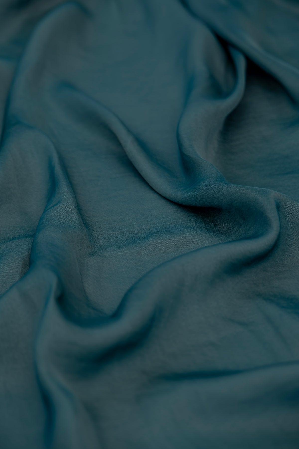 A close-up of draped teal green fabric with soft folds and a subtle woven texture.
