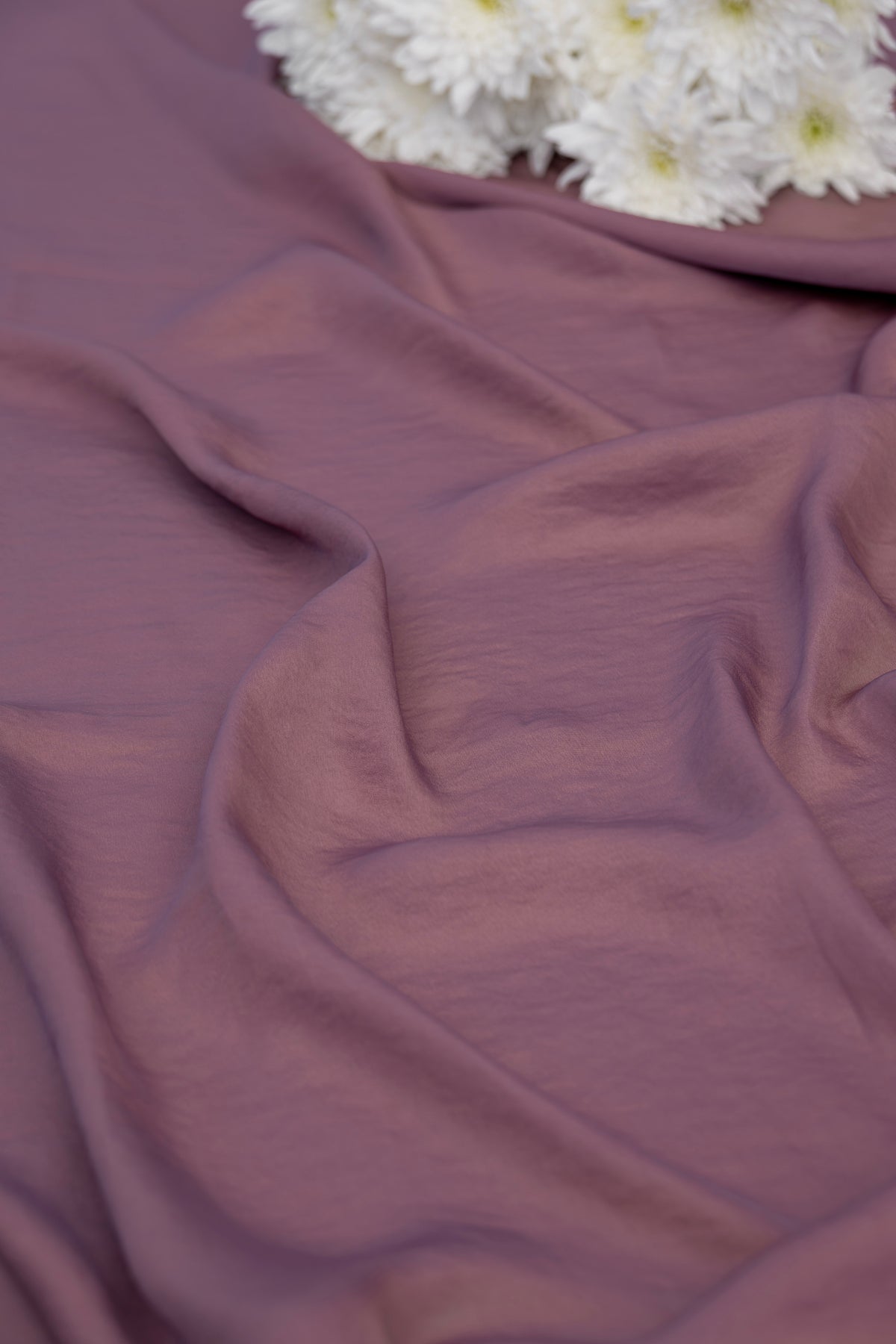 A close-up of draped dusty mauve fabric with soft folds, with a small cluster of white flowers at the top edge.