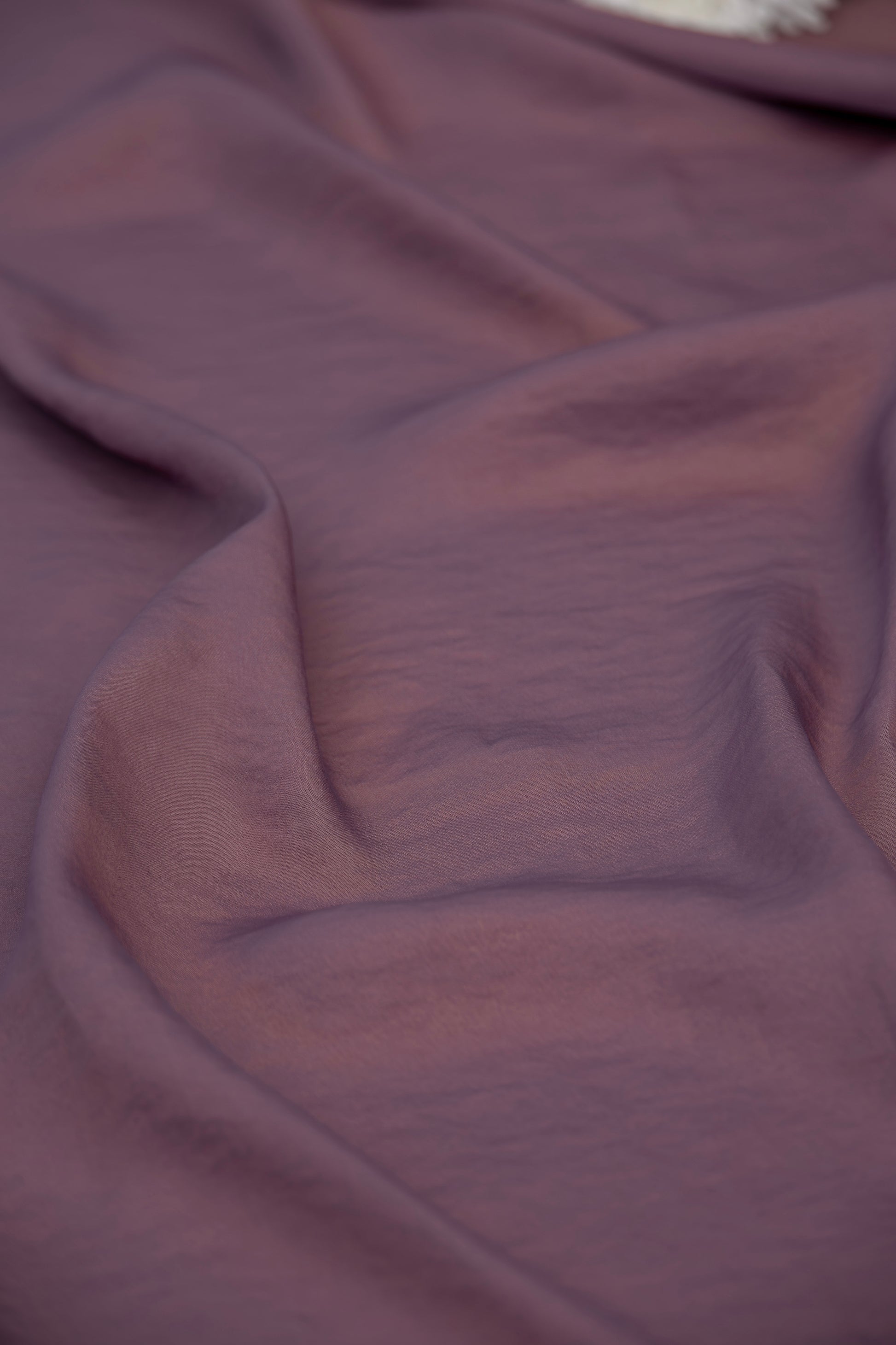 A close-up of draped mauve-purple fabric with soft folds and a subtle sheen.