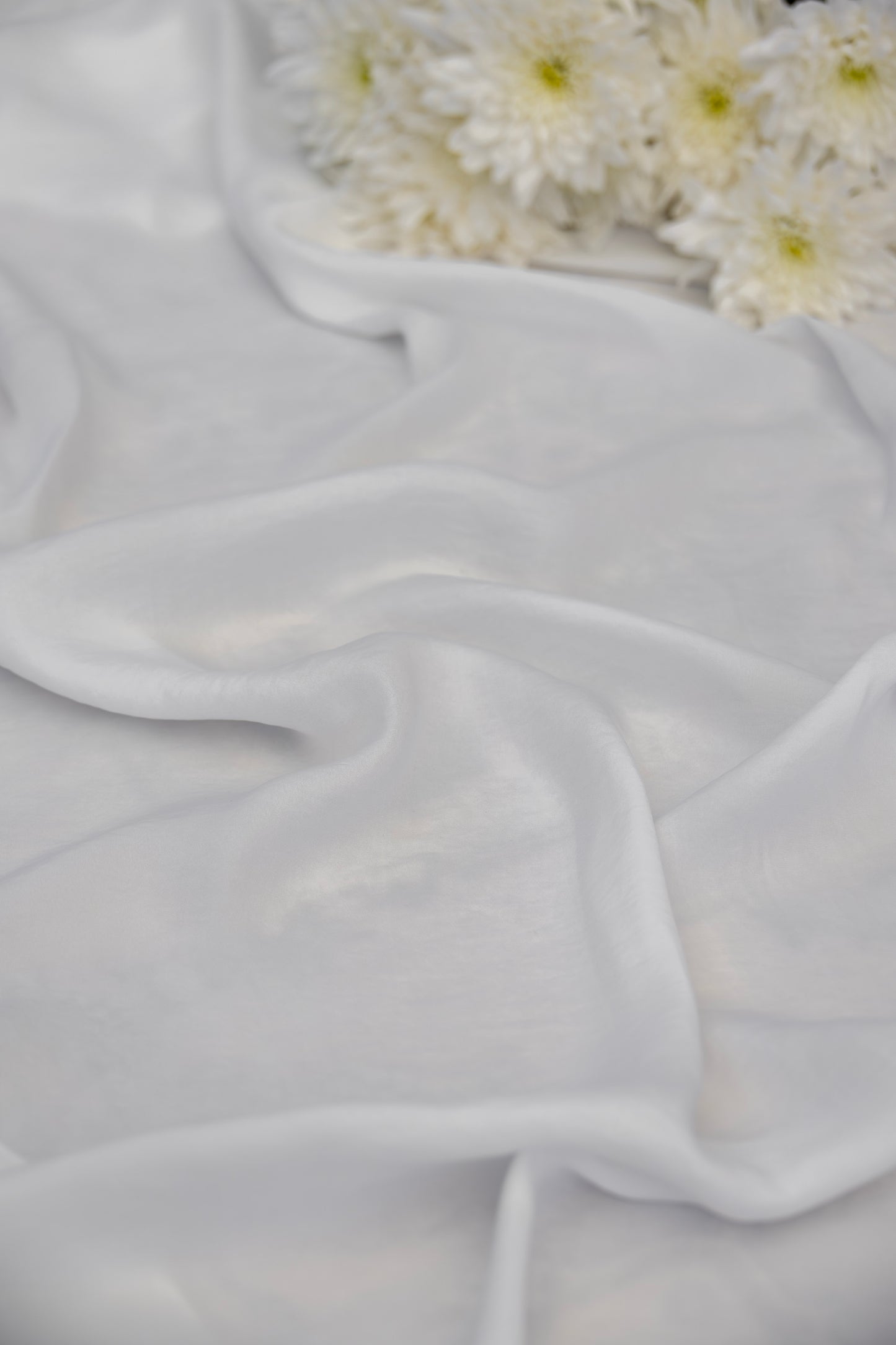 White sheer chiffon fabric draped in soft folds, with white daisies placed in the upper right corner.
