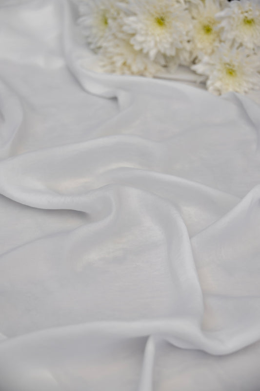 White sheer chiffon fabric draped in soft folds, with white daisies placed in the upper right corner.