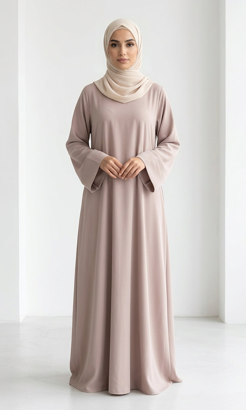 Woman wearing a long, beige colour dress and hijab standing in an indoor setting.