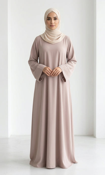 Woman wearing a long, beige colour dress and hijab standing in an indoor setting.