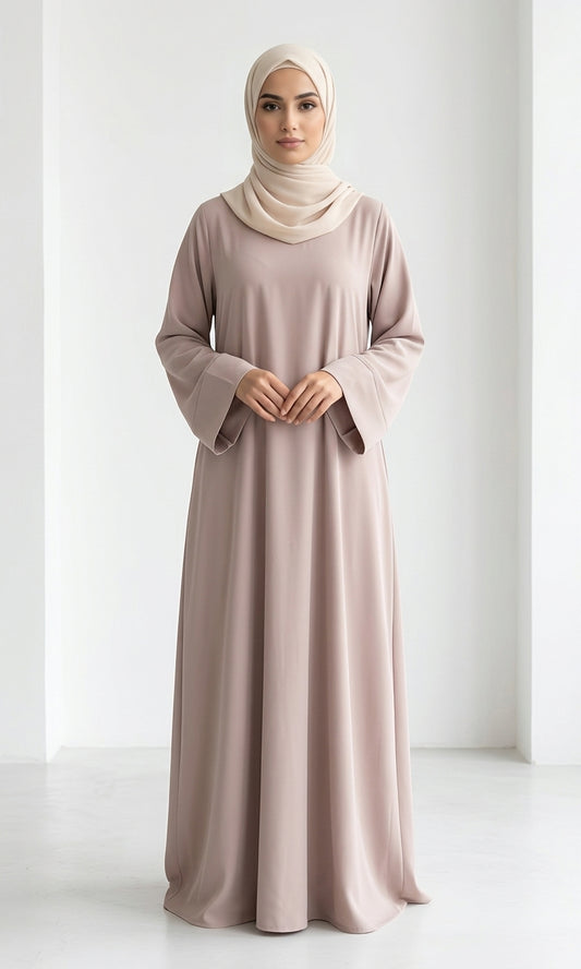 Woman wearing a long, beige colour dress and hijab standing in an indoor setting.
