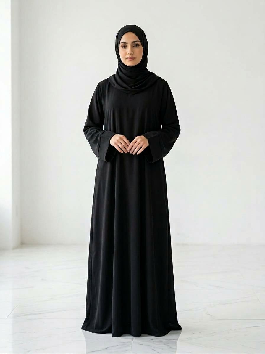 Woman wearing a long, black colour dress and hijab standing in an indoor setting.
