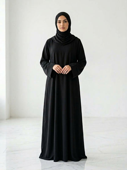 Woman wearing a long, black colour dress and hijab standing in an indoor setting.