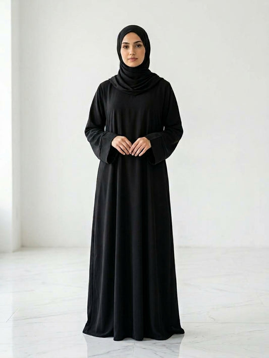 Woman wearing a long, black colour dress and hijab standing in an indoor setting.