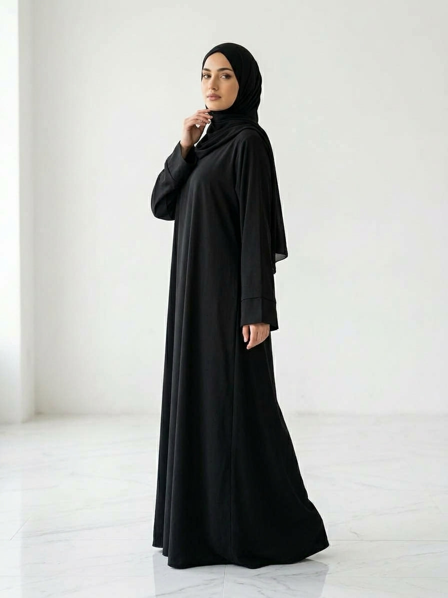 Woman wearing a long, black colour dress and hijab standing in an indoor setting.