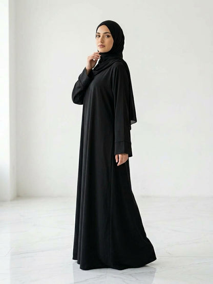 Woman wearing a long, black colour dress and hijab standing in an indoor setting.