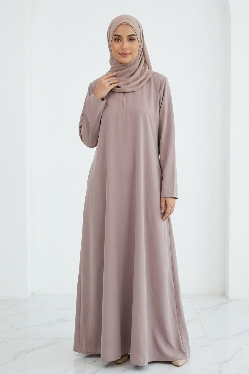 Woman wearing a long, light-colored dress and hijab standing in an indoor setting.