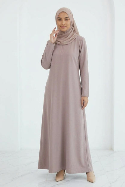 Woman wearing a long, light-colored dress and hijab standing in an indoor setting.